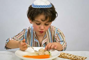 Un garçon juif avec une kippa sur la tête tout en mangeant des boulettes de pain azyme et du pain sans levain.