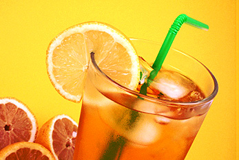 Un verre de thé glacé avec des citrons frais et de la paille verte sur fond jaune.