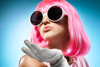 Une jeune femme avec de grandes lunettes noires, gants blancs et cheveux roses.